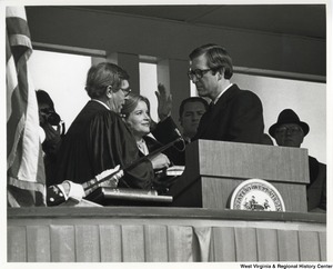 ["Governor Jay Rockefeller taking the oath of office  for the second time by the Honorable Sam R. Harshbarger, Chief justice of the Supreme Court of Appeals of West Virginia, as Sharon Rockefeller looks on."]%